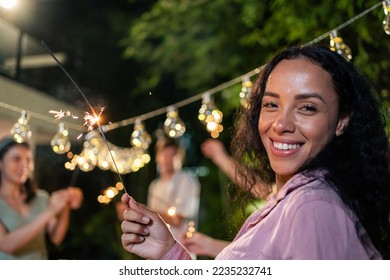 Portrait of Latino woman looking at camera while having party outdoor. Attractive beautiful girl having dinner, eating foods, celebrate weekend reunion gathered together with family at dining table. - Powered by Shutterstock