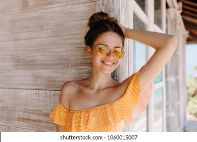 Portrait of laughing ecstatic lady with brown hair enjoying vacation at resort. Photo of inspired tanned woman expressing happiness while standing near wooden house. - Powered by Shutterstock