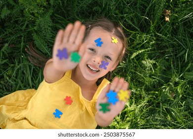 Portrait Of A Laughing Girl. The face and palms are covered with colored paper puzzles.  A symbol of awareness about autism. View from above - Powered by Shutterstock