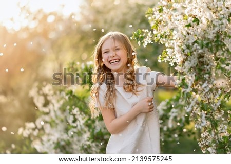 Portrait of laughing girl under falling petals of cherry blossom flowers in spring.