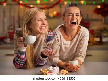 Portrait of laughing girlfriends having christmas snacks in christmas decorated kitchen - Powered by Shutterstock