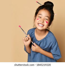 Portrait laughing happy brunette chinese girl and painted red hearts cheeks and brush in hair   hand over yellow wall background  Trendy children fashion  asian outfit concept