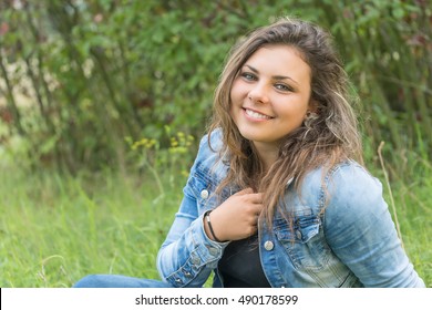 Portrait of laughing head tilted back teenage girl sitting outdoors. Girl is looking at the camera. 