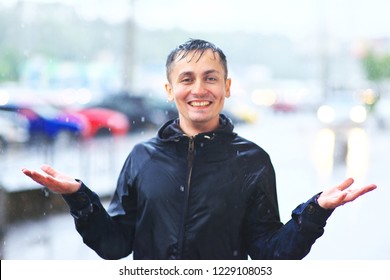 Portrait of a laughing man in a raincoat enjoying rain. catches raindrops up with his palms. Bad stormy rainy weather concept Waterproof wear concept. sun mood big luck life very good idea job win off