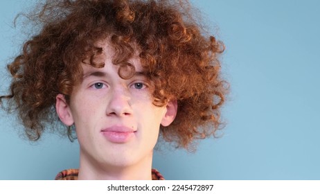 Portrait of a laughing red-haired curly-haired teenage boy with braces on his teeth isolated on a blue studio portrait background. 4k video - Powered by Shutterstock