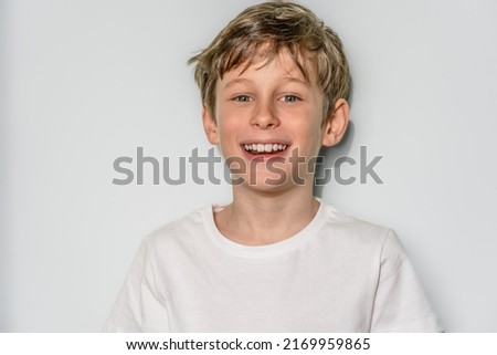 Portrait of a laughing white Eastern European 9 year old boy wearing a white t-shirt. The child looks directly into the camera with a smile. copy space on the left