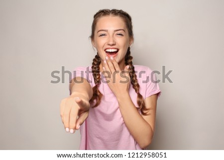 Portrait of laughing young woman pointing at viewer on light background