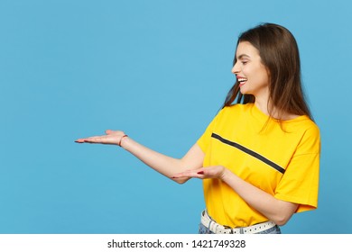 Portrait of laughing young woman in vivid casual clothes looking, pointing hands aside, hold something isolated on bright blue wall background in studio. People lifestyle concept. Mock up copy space - Shutterstock ID 1421749328