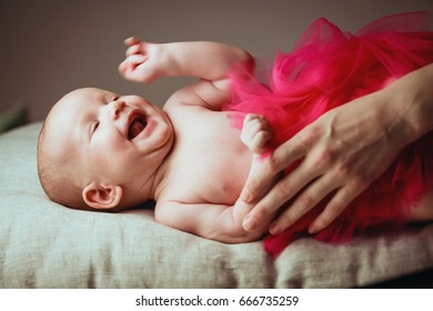 Portrait a laughs very loudly cute little 1-2 month old baby on pillow in ballerina skirt