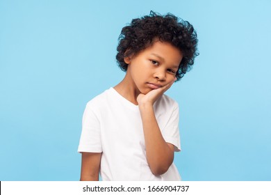 Portrait of lazy bored preschool boy with curly hair leaning on hand and looking depressed, child with indifferent gloomy expression has no energy. indoor studio shot isolated on blue background - Powered by Shutterstock