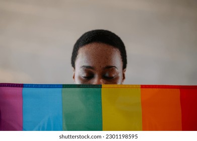 Portrait of a lesbian African American woman with closed eyes posing with gay pride, rainbow flag while peeking out from behind. LGBTQ concept. Focus on a half face of a black female that is visible. - Powered by Shutterstock