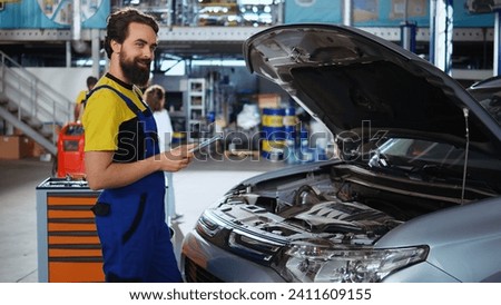 Portrait of licensed technician in auto repair shop doing car routine checkup using tablet, looking for damages. Certified mechanic in garage checking to see if vehicle components need to be changed