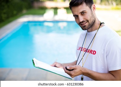 Portrait of lifeguard holding clipboard and stopwatch at poolside on a sunny day - Powered by Shutterstock