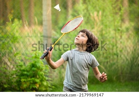 Portrait of little adorable boy playing badminton in yard outdoors in summer