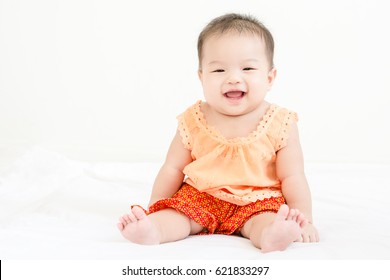 Portrait of a little adorable infant baby girl sitting on the bed and smiling to camera with copyspace - Shutterstock ID 621833297