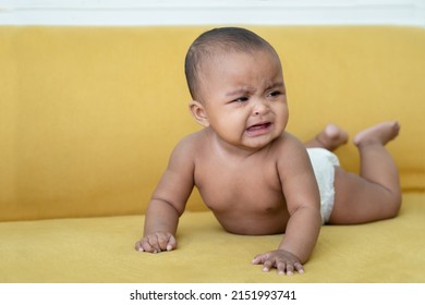 Portrait of Little African newborn baby girl wear diaper crying and tears drop from her eye while crawling on yellow sofa at home. Innocent infant expression. White background