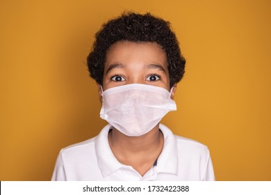 Portrait of little afro boy with medical face mask looking at camera. Child wearing protective mask from virus . Coronavirus and pandemic concept. 