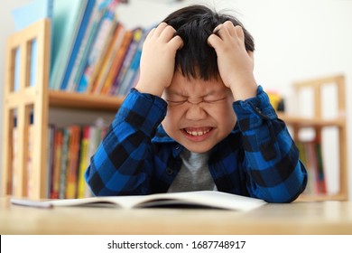 Portrait Of Little Asian Boy Frustrated Over School Work With His Both Hand On Head. Boy Studying At Table At Home