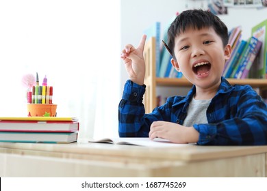 Portrait Of Little Asian Boy Pointing Finger While Reading, Sitting At Desk And Doing Homework. Education Concept.