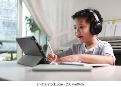Portrait of a little Asian boy using tablet computer and headphone during pandemic lockdown, homeschooling, social distance, stay at home, online education concept