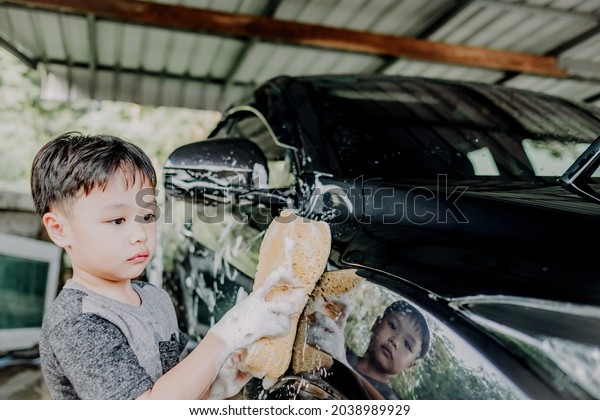 Portrait of little asian boy washing a car on a\
sunny day. Soft focus. Copy\
space.
