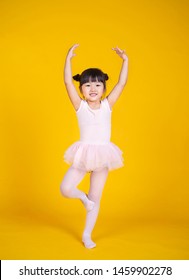 Portrait of little asian child girl dreams of becoming ballerina in a pink tutu skirt isolated on yellow background. Happy young girl practise her dance. Education childhood toddler lifestyle concept