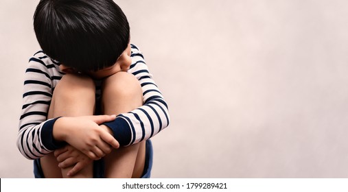 Portrait Of Little Asian Child Sit Alone, Hug Knees, Lay His Face On His Legs And Look Away. Autism Spectrum Awareness, Child Emotional Development And Stress And Depression In Early Childhood Concept