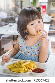 Portrait of little asian girl in fast food restaurant eating fastfood lunch, Happy little asian girl eating a french fries, close up 