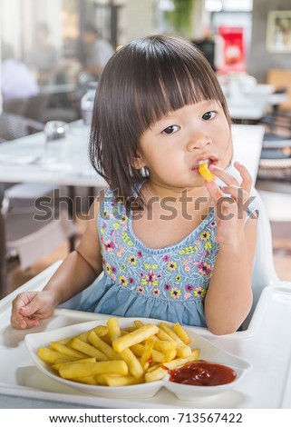 Portrait of little asian girl in fast food restaurant eating fastfood lunch, Happy little asian girl eating a french fries, close up 