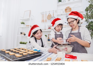 Portrait Of Little Asian Girl Sisters And Her Mother Baking Cooking Cake And Cookies In The Kitchen Christmas Eve Holiday Celebration. Happy Family Together Holiday Education Concept