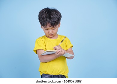 Portrait of little Asian kid student with pencil and notebook, isolated on blue background - Shutterstock ID 1640595889