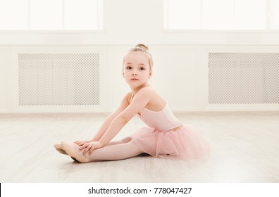 Portrait of little ballerina on floor, copy space. Smiling baby girl dreaming to become professional ballet dancer, classical dance school