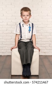 Portrait Of A Little Blond Child Boy Sitting On A Soft Chair In The White Brick Wall