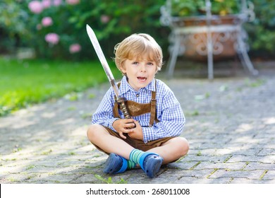 Portrait of little blond kid boy with toy sword, outdoors. On warm sunny summer day.