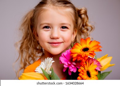 portrait of a little blonde girl with a bouquet of spring flowers on a light background. child in orange dress holding a bouquet of tulips in his hands. space for text. spring concept - Powered by Shutterstock