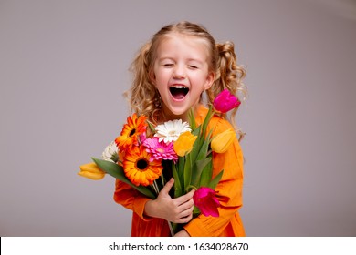 portrait of a little blonde girl with a bouquet of spring flowers on a light background. child in orange dress holding a bouquet of tulips in his hands. space for text. spring concept - Powered by Shutterstock
