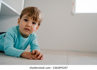 Portrait Of A Little Boy In Blue At Home Lying In The Book Shelf On The Floor Hiding Games