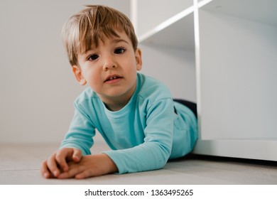 Portrait Of A Little Boy In Blue At Home Lying In The Book Shelf On The Floor Hiding Games