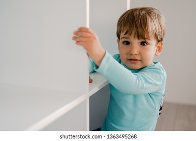 Portrait Of A Little Boy In Blue At Home Standing In The Book Shelf