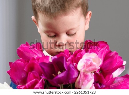 Portrait of a little boy with a bouquet of beautiful pink and purple flowers. A child carries flowers as a gift, Mother's Day, March 8, Valentine's Day. Postcard, child with flowers. A boy sniffs