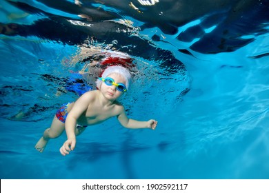 Portrait of a little boy in a Christmas hat and glasses in a pool under water. He looks at the camera. Baby learns to dive. Swimming lessons with a child. Healthy lifestyle. Horizontal orientation