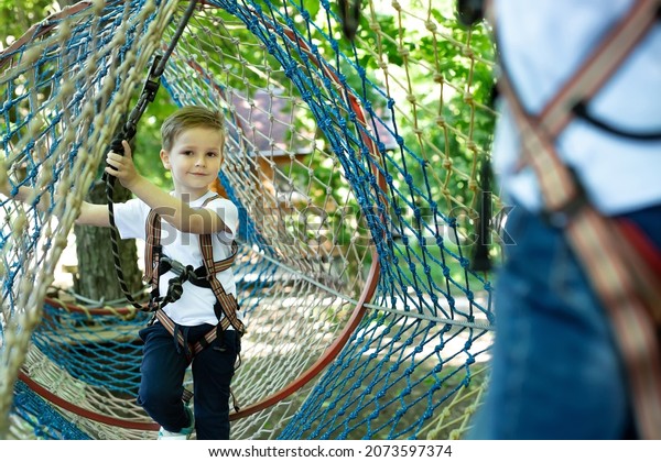 Portrait of a little boy in climbing gear\
in a rope park, holding a rope with a\
carbine.