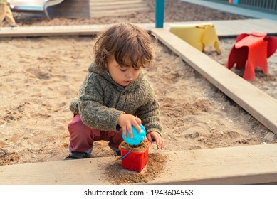 Portrait of a little boy with long hair playing in the sandbox at the playground outdoors
