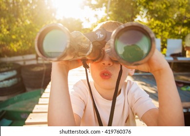 Portrait of little boy looking through binoculars on river bank. Cute kid with binoculars sitting on the pier on river. Focus on child. - Powered by Shutterstock