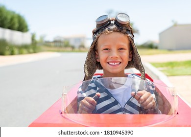 Portrait Of Little Boy Riding An Handmade Toy Car On Street With Hands On Steering Wheel Ready For The Race. Smiling Funny Kid Rides On A Go-kart Looking At Camera With Copy Space Outdoor.