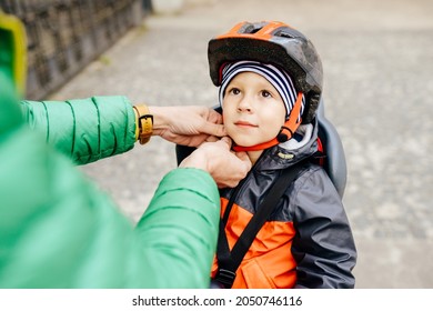 Portrait Of Little Boy With Security Helmet On The Head Sitting In Bike Seat And Her Father With Bicycle. Safe And Child Protection Concept. Fathers Hands Putting Helmet On Cute Little Son.