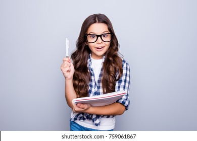 Portrait of little, brunette, cute, smiling girl holding notebook raising her pencil up, finding a solution how to do exercise, standing over grey background - Powered by Shutterstock