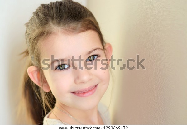 portrait\
of a little caucasian white beautiful brunette girl with pony tail\
on neutral background. smiling green eyed happy girl with cute\
protruding ears. Kid expression attractive\
face