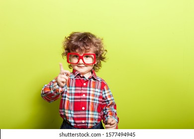 Portrait Of A Little Curly Boy In Glasses On A Bright Green Background. Little Scientist, Inventor, Researcher, Physicist, Mathematician.