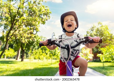 Portrait little cute adorable caucasian toddler boy in safety helmet enjoy having fun riding exercise bike in city park road yard garden forest. Child first bike. Kid outdoors sport summer activities - Shutterstock ID 2002363478